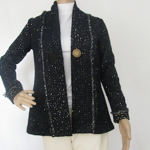 Puede incluir: Una chaqueta negra de tweed con un botón dorado y un cuello blanco. La chaqueta tiene un dobladillo ligeramente acampanado y está forrada con una tela negra.