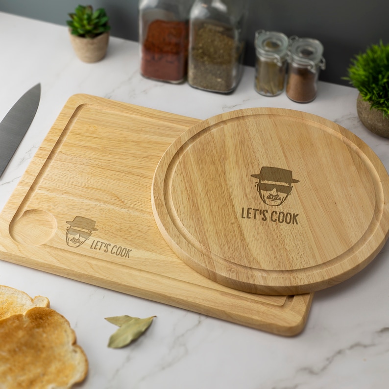 May include: A wooden cutting board set with a round and rectangular board. Both boards feature a cartoon image of a man wearing a hat and sunglasses with the text "Let's Cook".