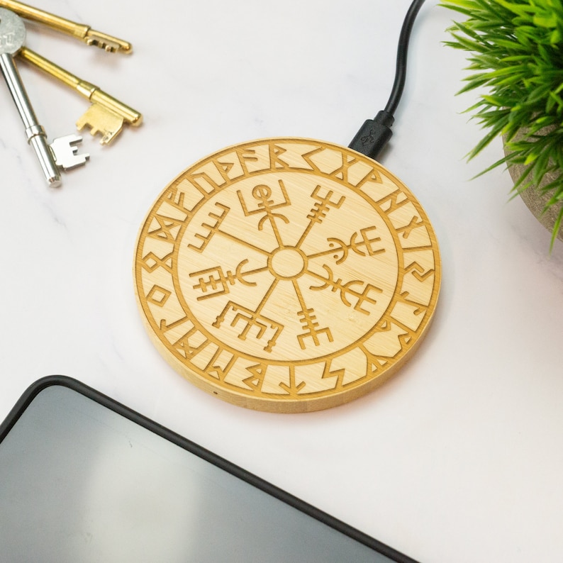 May include: A wooden wireless charging pad with a circular design featuring a compass rose and runes around the edge. The charging pad is connected to a USB cable.