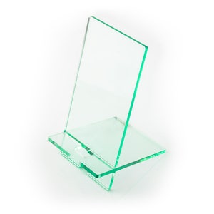 May include: A clear green acrylic phone stand with a rectangular base and a taller rectangular back panel. The stand is designed to hold a phone upright.