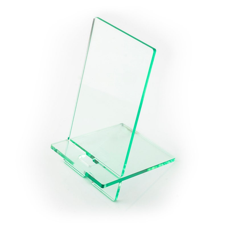 May include: A clear green acrylic phone stand with a rectangular base and a taller rectangular back panel. The stand is designed to hold a phone upright.