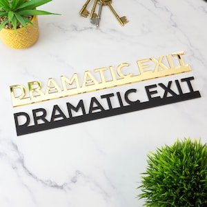 K&ouml;nnte beinhalten: Ein goldenes Acrylschild mit Spiegelfl&auml;che mit dem Text "Dramatic Exit" auf einem schwarzen Acrylschild mit dem gleichen Text.