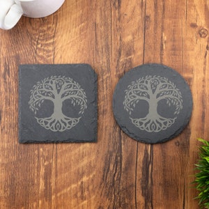 Peut inclure: Deux sous-verres en ardoise avec un motif d'arbre de vie. Les sous-verres sont gris et présentent un arbre détaillé avec des racines et des branches.