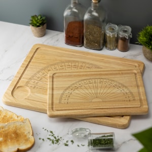 May include: Two wooden cutting boards with protractor markings. The larger board has a protractor on the left side and the smaller board has a protractor in the center. Both boards are made of light brown wood.