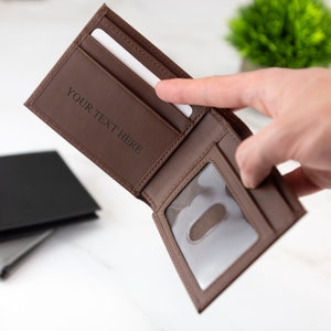 May include: A brown leather wallet with a clear plastic window for an ID card. The wallet is open and has a slot for credit cards and a space for cash. The wallet is personalized with the text "YOUR TEXT HERE".
