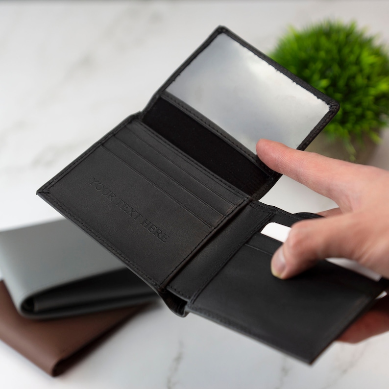 May include: Black leather wallet with multiple card slots and a clear ID window. The wallet is open and has the text "YOUR TEXT HERE" embossed on the front.
