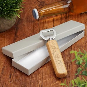 May include: A wooden bottle opener with a metal opener and a personalized inscription that reads "Classic Home Est. 2015". The bottle opener is in a gray box.