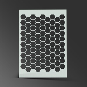 May include: A white stencil with a black honeycomb pattern. The stencil is made of a thin, flexible material and is designed for use with paint or other mediums.