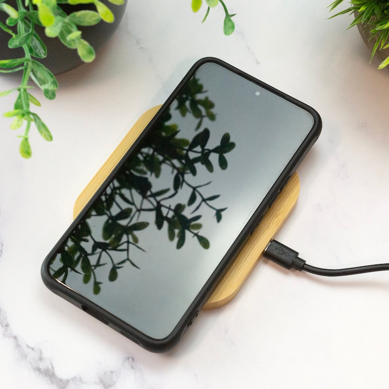 May include: A black smartphone is charging on a wooden wireless charging pad. A black charging cable is connected to the pad.