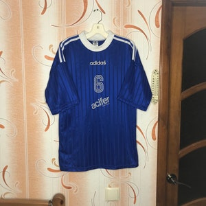 Peut inclure: Maillot de football bleu avec des rayures blanches et le logo Adidas. Le numéro 6 et le mot "acifer" sont imprimés sur le devant du maillot.