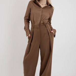 May include: A brown long-sleeved shirt with a button-up collar and a pair of wide-leg brown pants. The person is wearing white sneakers.