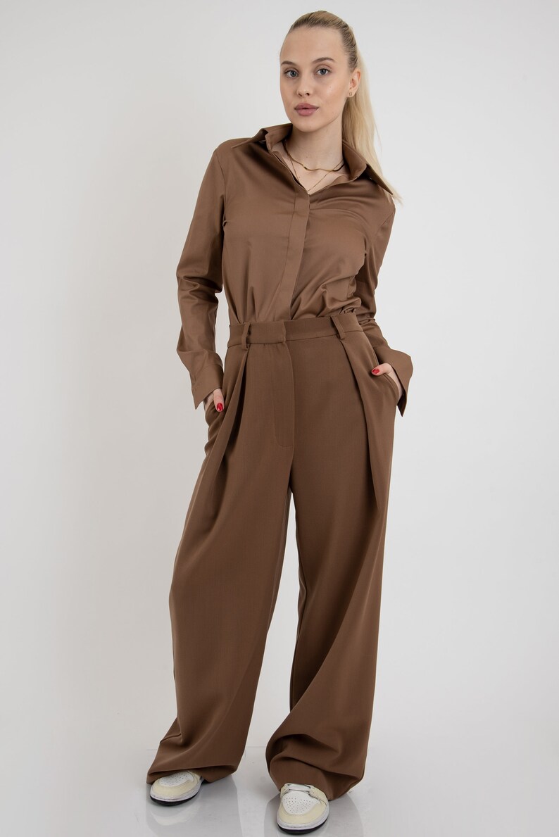 May include: A brown long-sleeved shirt with a button-up collar and a pair of wide-leg brown pants. The person is wearing white sneakers.