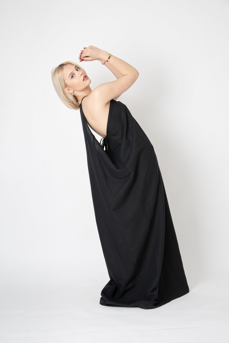 Pode incluir: Uma mulher vestindo um vestido maxi preto com um decote drapeado. O vestido &eacute; sem mangas e tem um caimento solto e fluido.