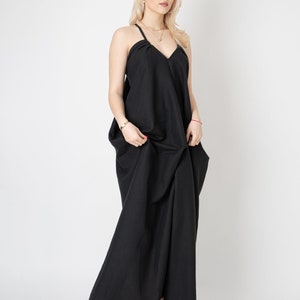 Pode incluir: Uma mulher vestindo um vestido maxi preto com decote em V e al&ccedil;as finas. O vestido &eacute; solto e tem uma silhueta fluida.