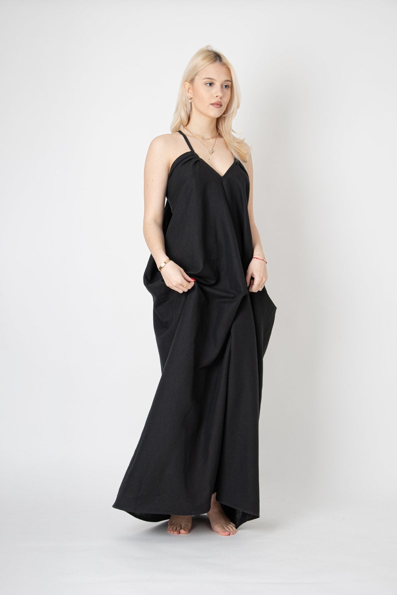 Pode incluir: Uma mulher vestindo um vestido maxi preto com decote em V e al&ccedil;as finas. O vestido &eacute; solto e tem uma silhueta fluida.