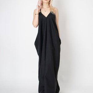 Pode incluir: Uma mulher vestindo um vestido maxi preto com decote em V e al&ccedil;as finas. Ela est&aacute; em p&eacute; em um fundo branco.