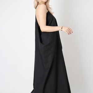 Pode incluir: Uma mulher vestindo um vestido maxi preto com uma silhueta solta e fluida. O vestido tem um design simples e elegante e &eacute; perfeito para uma ocasi&atilde;o casual ou formal.