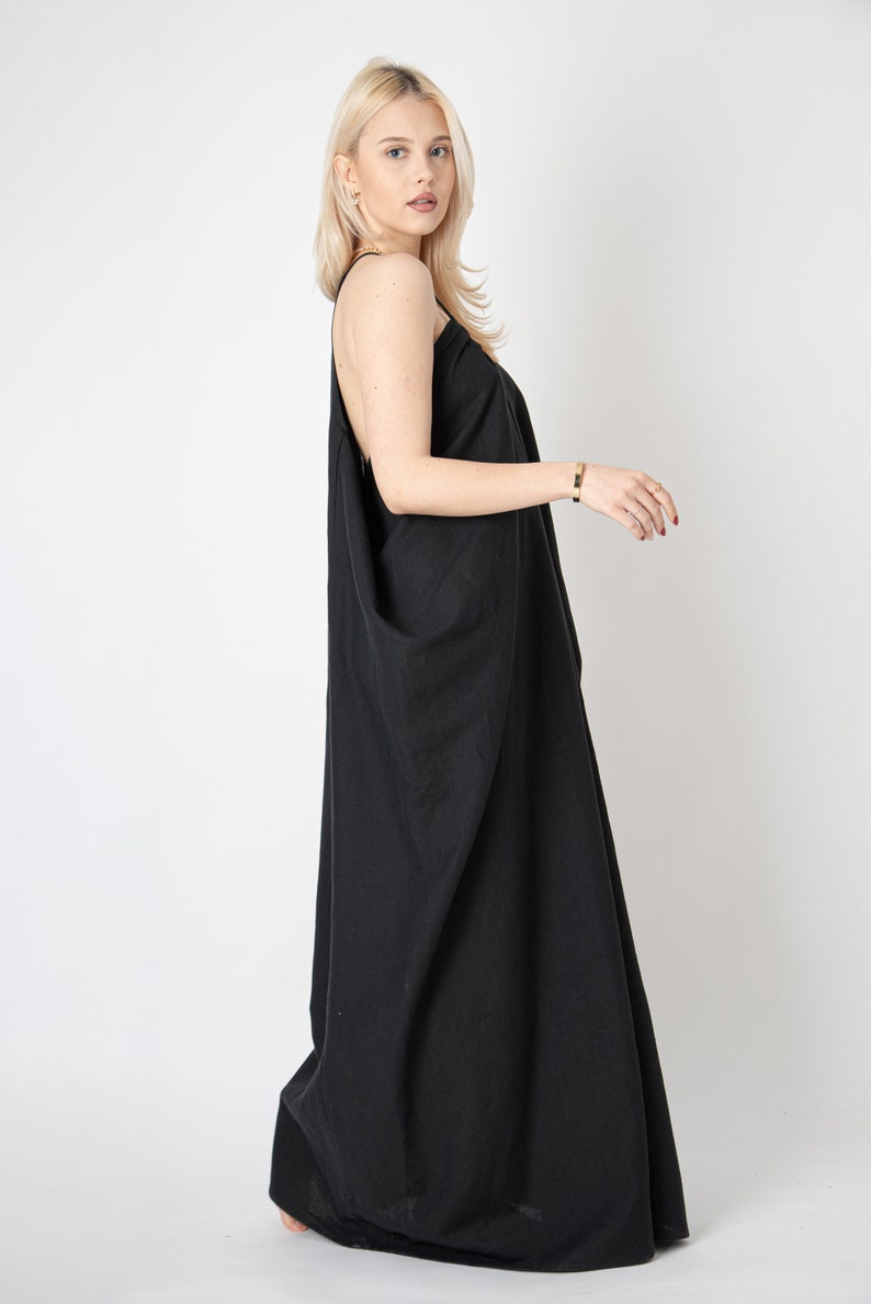 Pode incluir: Uma mulher vestindo um vestido maxi preto com uma silhueta solta e fluida. O vestido tem um design simples e elegante e &eacute; perfeito para uma ocasi&atilde;o casual ou formal.