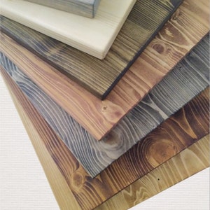 May include: A stack of six wooden boards in various shades of brown, grey, and natural wood. The boards are arranged in a staggered pattern, with the top board being the lightest colour and the bottom board being the darkest colour.