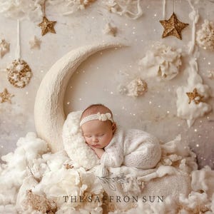 May include: A sleeping baby in a white outfit and headband rests on a fluffy white pillow in a crescent moon prop. The background includes clouds, stars, and the text "THE SAFFRON SUN". The scene evokes a dreamy, celestial theme.