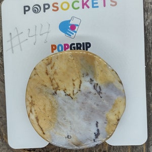 May include: A round, beige and white marble-patterned phone grip with a PopGrip logo. The grip is on a white background with the text "#44" and "POPSOCKETS" written above it.