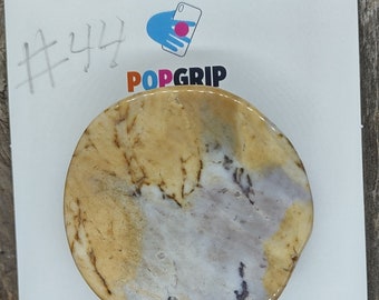 May include: A round, beige and white marble-patterned phone grip with a PopGrip logo. The grip is on a white background with the text "#44" and "POPSOCKETS" written above it.