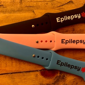 May include: Three Apple Watch bands in black, pink, and blue with the word "Epilepsy" and a red star printed on each.