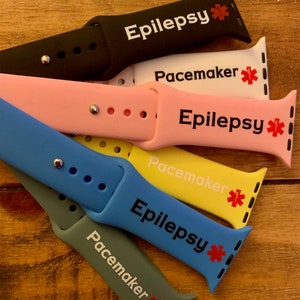Könnte beinhalten: Ein Set aus sechs bunten Silikon-Apple Watch-Armbändern mit medizinischem Warnhinweis. Die Armbänder sind schwarz, rosa, gelb, blau und grau. Jedes Armband hat einen roten Stern und den Text "Epilepsie" oder "Herzschrittmacher".