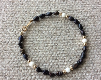 May include: A black and white beaded bracelet with gold accents. The bracelet is made of small, round beads and has a clasp closure.
