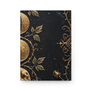 May include: A black hardcover journal featuring a gold embossed design of three lunar phases on the left side, surrounded by intricate gold vines, thorns, and rosebuds. The dark background is accented with small gold stars and subtle wisps of smoke.