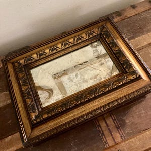 May include: A vintage gold-toned framed mirror with ornate detailing. The mirror has a crack in the glass.