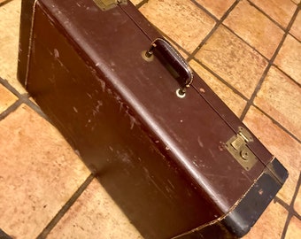 May include: A vintage brown leather suitcase with brass hardware and a leather handle. The suitcase has a worn look and is in good condition.