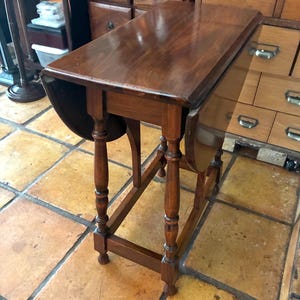 May include: A dark brown wooden drop-leaf table with a rectangular top and two hinged side leaves. The table features four turned legs connected by a rectangular base stretcher, showcasing a polished wood grain finish throughout the structure.