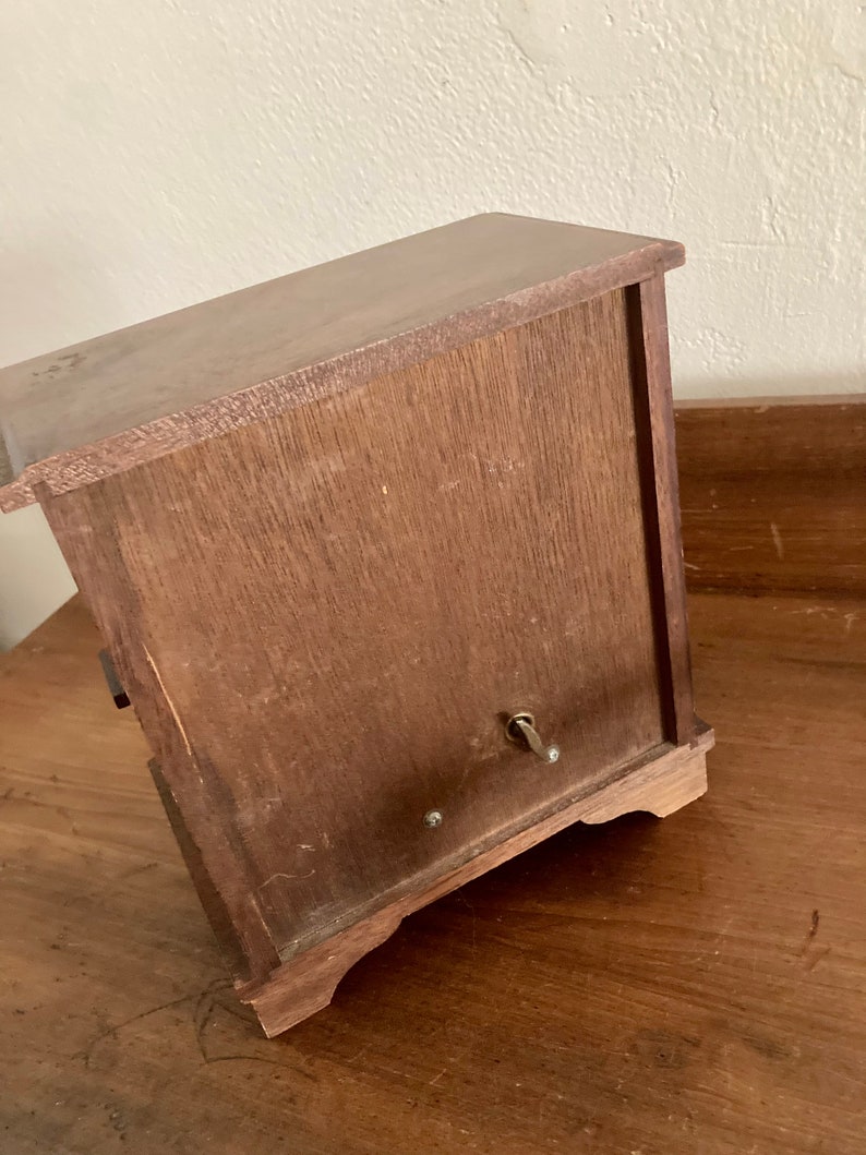 May include: A wooden music box with a winding key on the side. The box has a dark brown finish and a simple design.