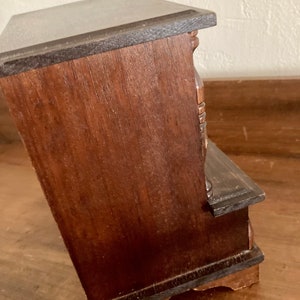 May include: A dark brown wooden jewelry box with a hinged lid and multiple drawers. The box has a decorative carved design on the front.