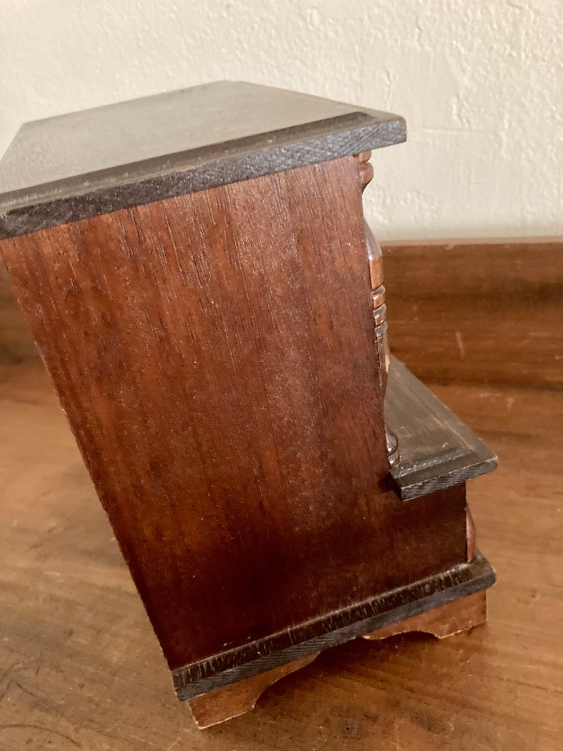 May include: A dark brown wooden jewelry box with a hinged lid and multiple drawers. The box has a decorative carved design on the front.