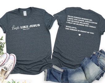 May include: A dark heather gray t-shirt with the text "Love Like Jesus John 15:13" on the front. The back of the shirt has the text "Dear person behind me, I hope you know Jesus loves you beyond measure. I pray he blesses you today. With love, the person in front of you".