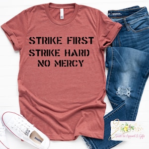 May include: A maroon t-shirt with the text "Strike First Strike Hard No Mercy" printed in black.