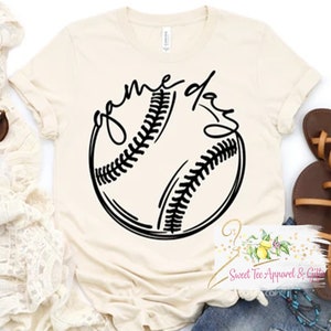 May include: A beige t-shirt with a black baseball graphic and the text "game day" in a cursive font.