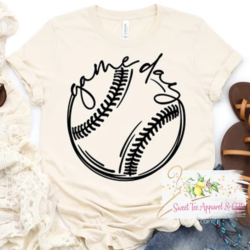May include: A beige t-shirt with a black baseball graphic and the text "game day" in a cursive font.