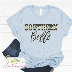 May include: Light blue t-shirt with the text "Southern Belle" in brown lettering. The word "Southern" is decorated with a floral pattern.