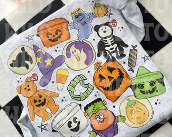 May include: A light gray sweatshirt featuring a colorful Halloween-themed graphic print. The design includes illustrations of a pumpkin, a ghost, a skeleton bear, a witch hat, candy corn, a spider, and various other festive seasonal characters.