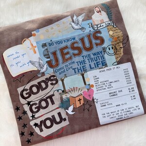 May include: Brown fabric with a collage design featuring the text "GOD'S GOT YOU" and "JESUS." The design includes doves, a cross, stars, and a receipt-like graphic with text. The overall theme is religious.