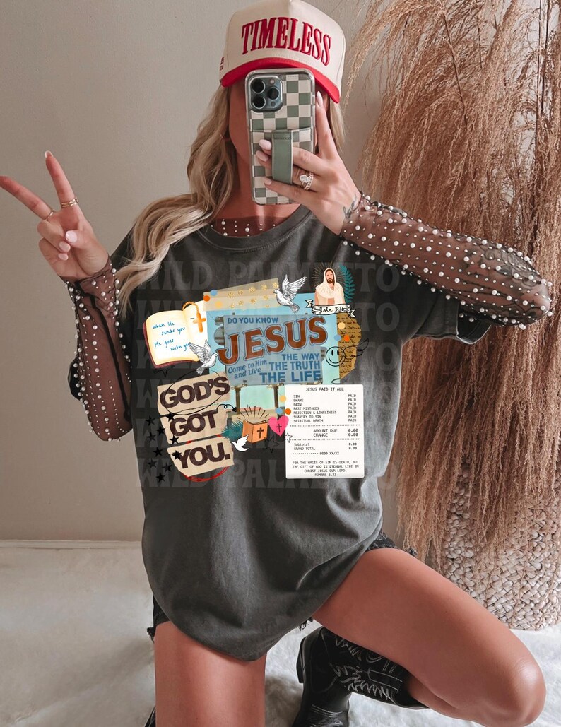 May include: A gray t-shirt with the text "GOD'S GOT YOU" and "DO YOU KNOW JESUS". The shirt has a graphic design with doves, a cross, and the words "THE WAY, THE TRUTH, THE LIFE". A red and white hat that says "TIMELESS" is also visible.