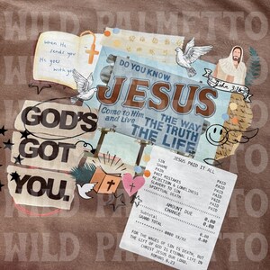 May include: Brown t-shirt with a collage design featuring religious imagery and text. The design includes the words "GOD'S GOT YOU," "JESUS," and a receipt that says "JESUS PAID IT ALL." Other elements include doves, a cross, and Bible verses.