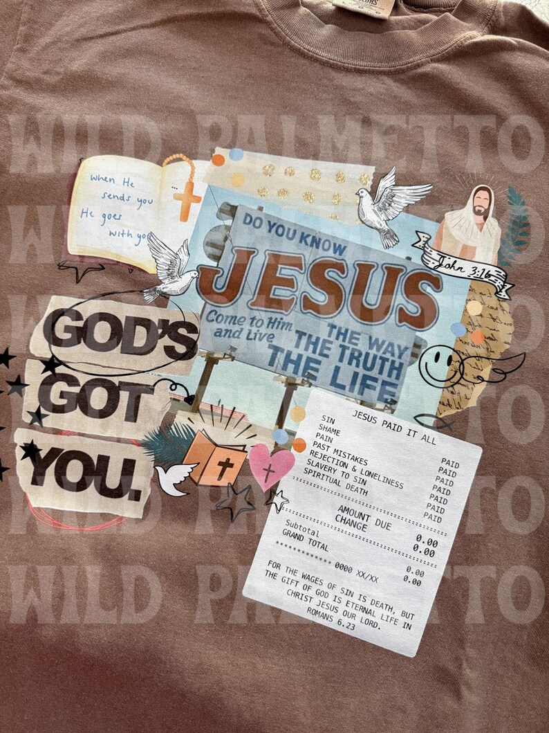 May include: Brown t-shirt with a collage design featuring religious imagery and text. The design includes the words "GOD'S GOT YOU," "JESUS," and a receipt that says "JESUS PAID IT ALL." Other elements include doves, a cross, and Bible verses.