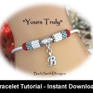 May include: A white beaded bracelet with red and green accents. The bracelet has a silver charm with the letter "B" on it. The bracelet is on a person's wrist and the text "Yours Truly" is above the bracelet.
