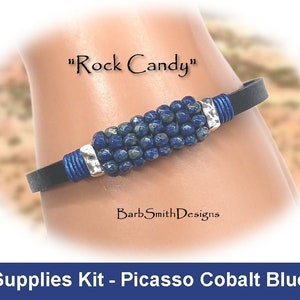 May include: A blue leather bracelet with a silver clasp and a row of blue Picasso Cobalt beads. The bracelet is labeled "Rock Candy".