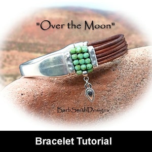 May include: A leather bracelet with a silver clasp and a turquoise bead accent. The bracelet is on a rock with the text "Over the Moon" and "Barb Smith Designs" above it. The text "Bracelet Tutorial" is below the image.
