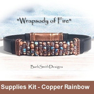 May include: A black leather bracelet with a copper and iridescent bead design. The bracelet has a magnetic clasp and the text "Wrapsody of Fire" is written above the bracelet. The text "BarbSmithDesigns" is written below the bracelet. The text "Supplies Kit - Copper Rainbow" is written below the bracelet.